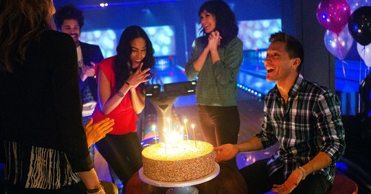 Birthday cake with candles surrounded by party guests on the lanes