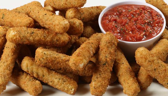 Pile of mozzarella sticks on a plate near a bowl of marinara sauce