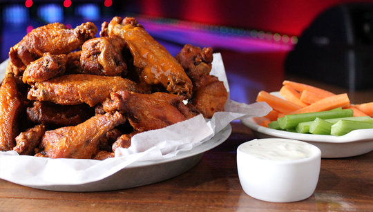 Basket of buffalo wings with a cup of dipping sauce and place of celery and carrots