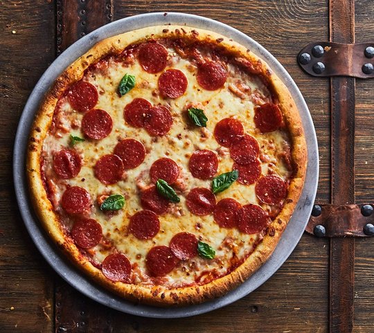 pepperoni pizza pie with basil on a wood surface